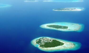 An aerial perspective of several lush green islands with white sand beaches surrounded by turquoise lagoons and deep blue ocean water in the Maldives.