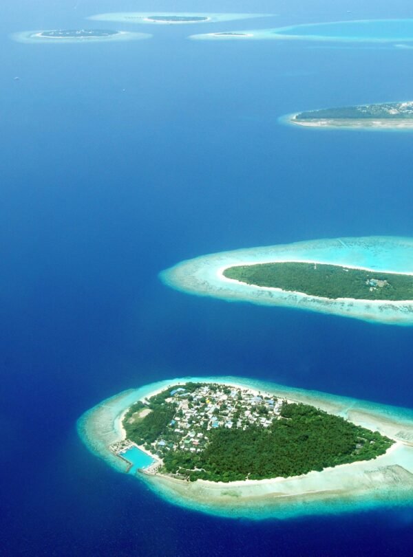 An aerial perspective of several lush green islands with white sand beaches surrounded by turquoise lagoons and deep blue ocean water in the Maldives.