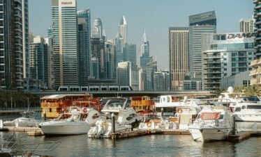 A ground-level view of several white yachts and traditional wooden dhows docked in the Dubai Marina canal.