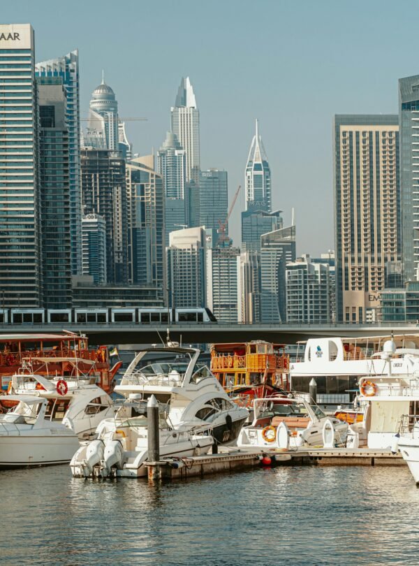 A ground-level view of several white yachts and traditional wooden dhows docked in the Dubai Marina canal.