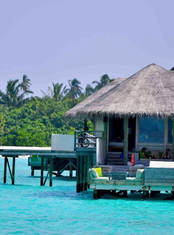 A close-up view of a luxury overwater villa with a thatched roof and light-colored wooden walls built on stilts over a vibrant turquoise lagoon.