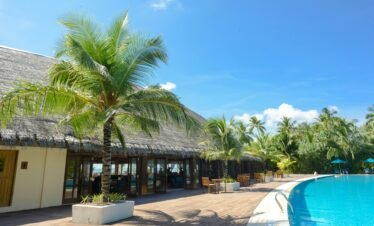A wide-angle shot of a large, curved swimming pool with clear blue water at a tropical resort.